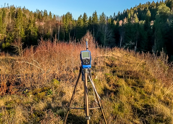 Ljudnivåmätare på stativ som mäter omgivningsljudnivån på ett lugnt lantligt fält omgivet av skog.